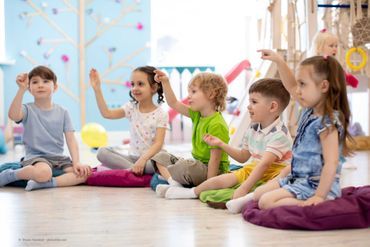 Kinder sitzen im Kreis und heben die Arme hoch
