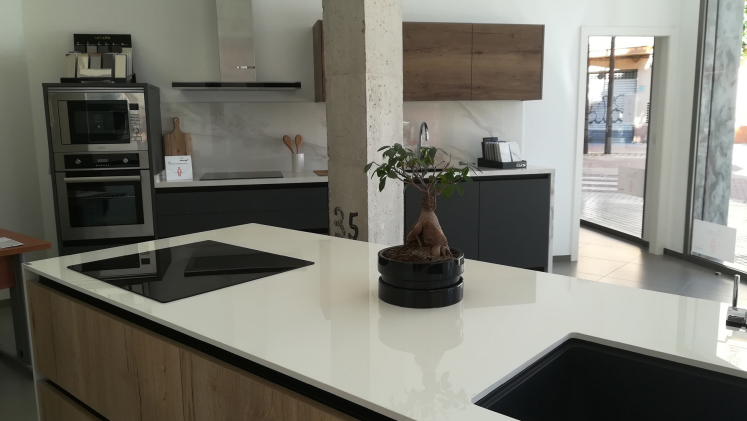 Cocina moderna con encimeras blancas, gabinetes oscuros y electrodomésticos de acero inoxidable.