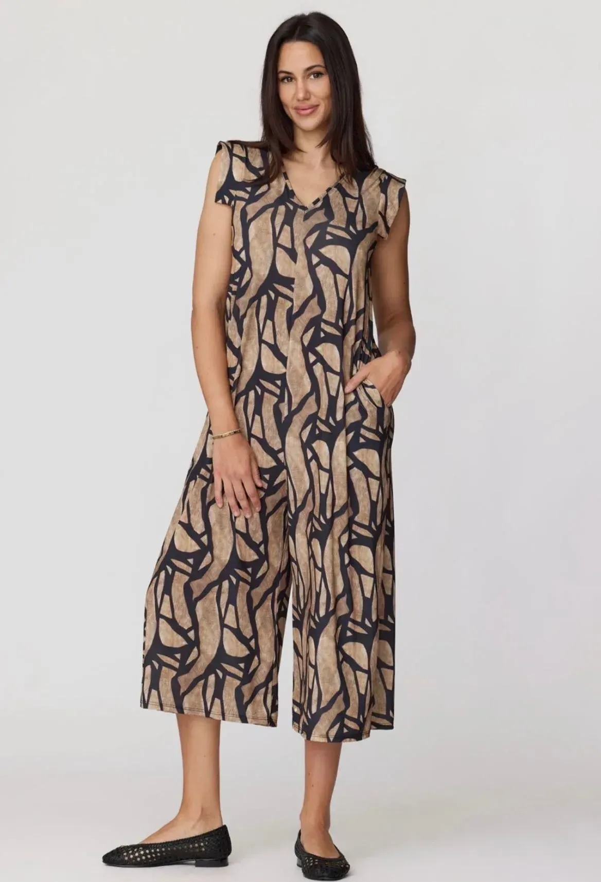 Modelo con un vestido midi sin mangas estampado en beige y negro y zapatos planos negros sobre un fondo liso.
