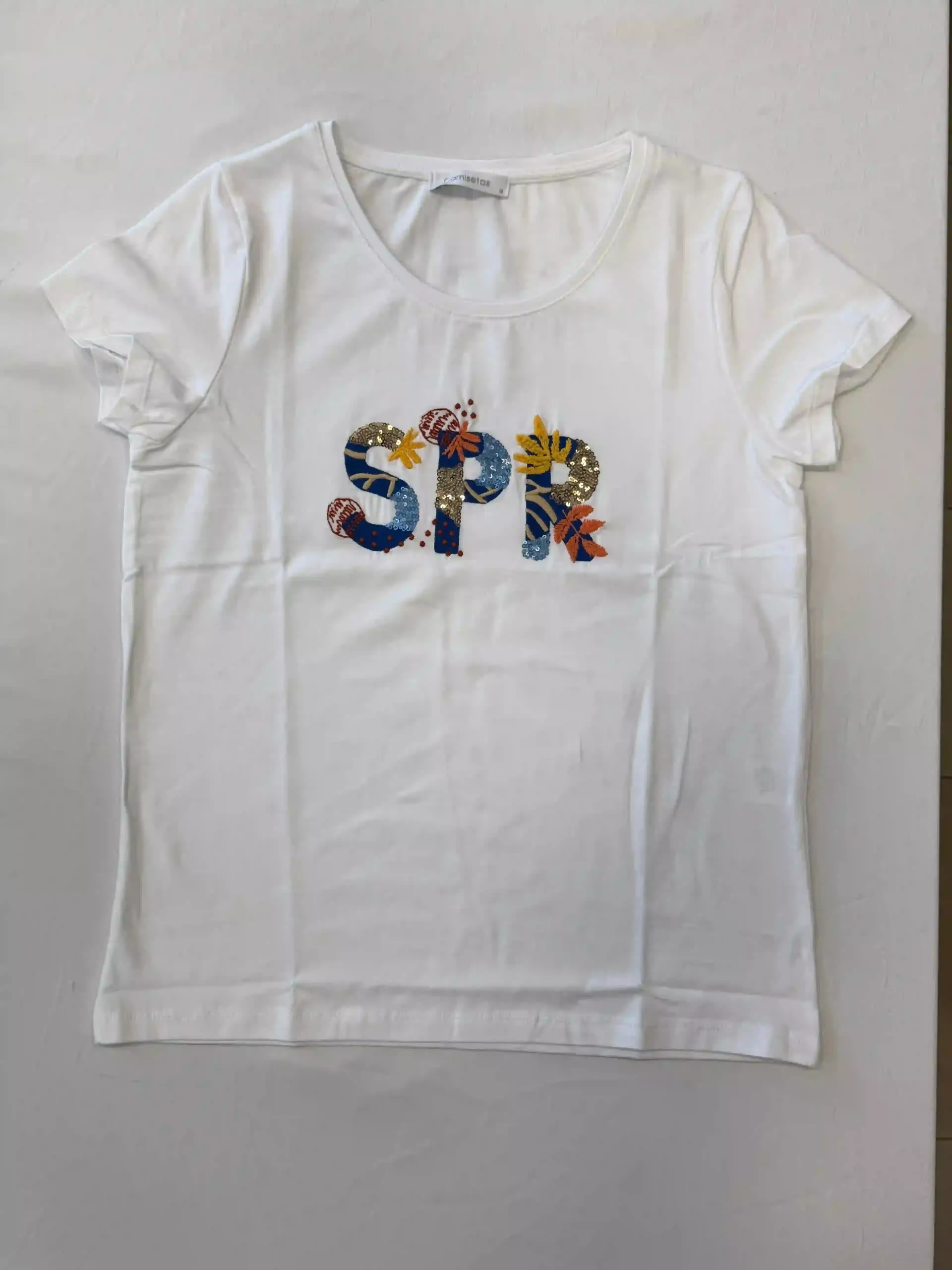 Camiseta blanca con las letras “SPR” de colores centradas en la parte delantera.