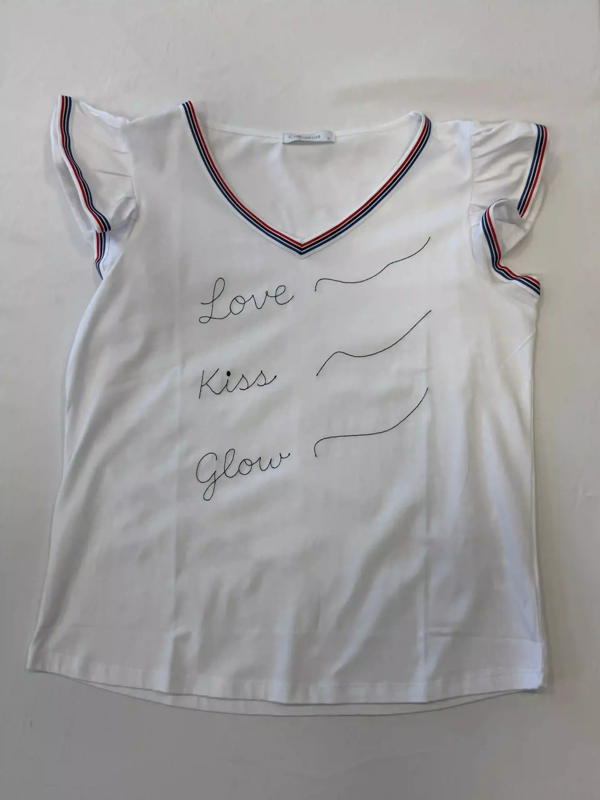 Camiseta blanca con cuello en V, ribete rojo y negro y texto decorativo en la parte delantera.
