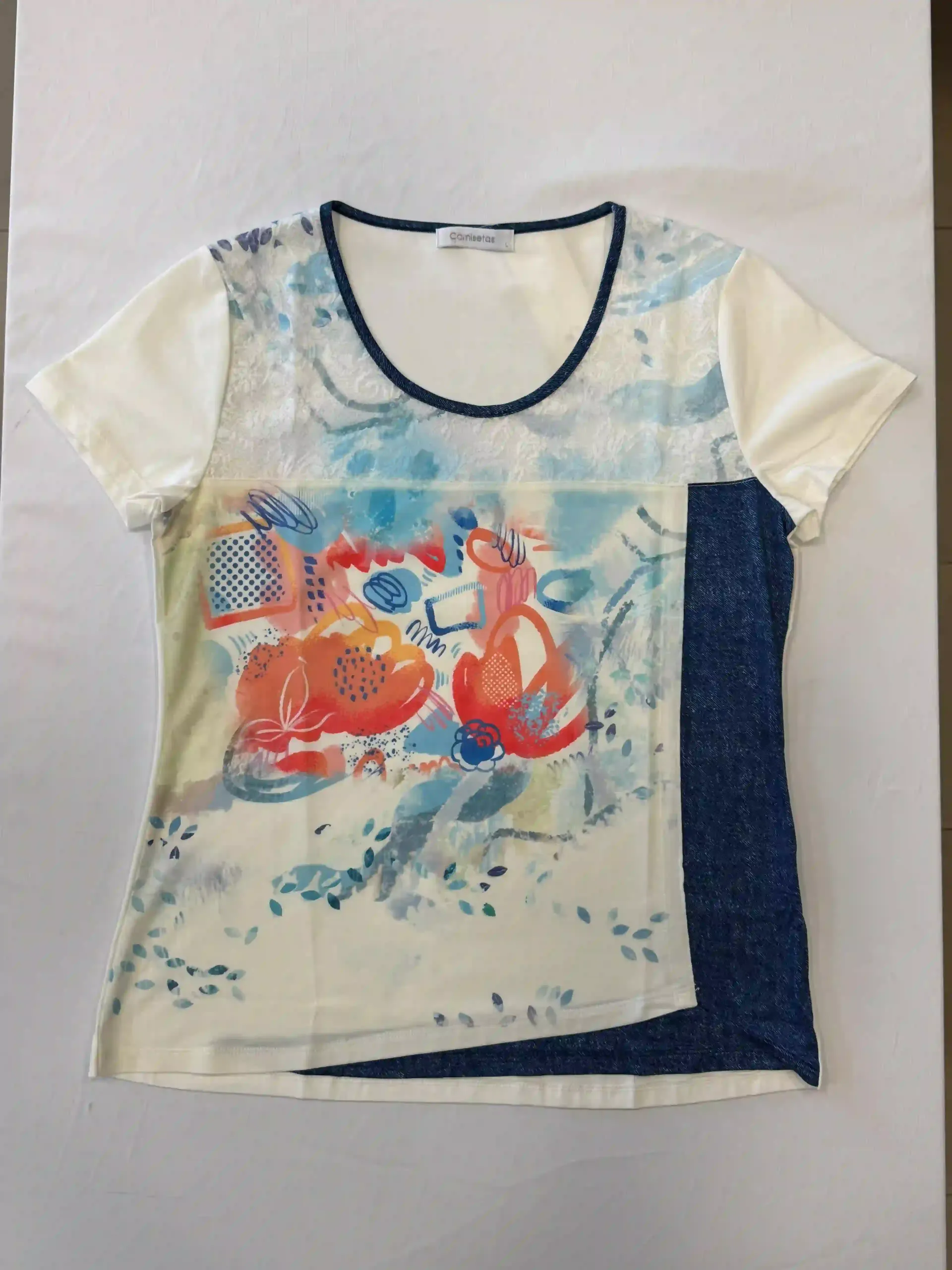 Camiseta blanca con estampado abstracto colorido y panel lateral azul marino extendida sobre una superficie blanca.