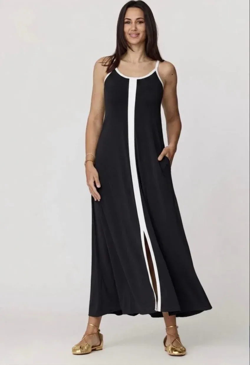 Mujer con un vestido largo negro sin mangas con ribete blanco, de pie sobre un fondo claro.