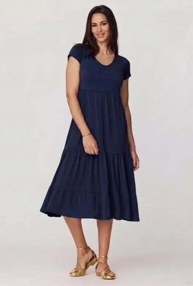 Mujer con vestido midi azul marino y sandalias doradas posando sobre un fondo claro.