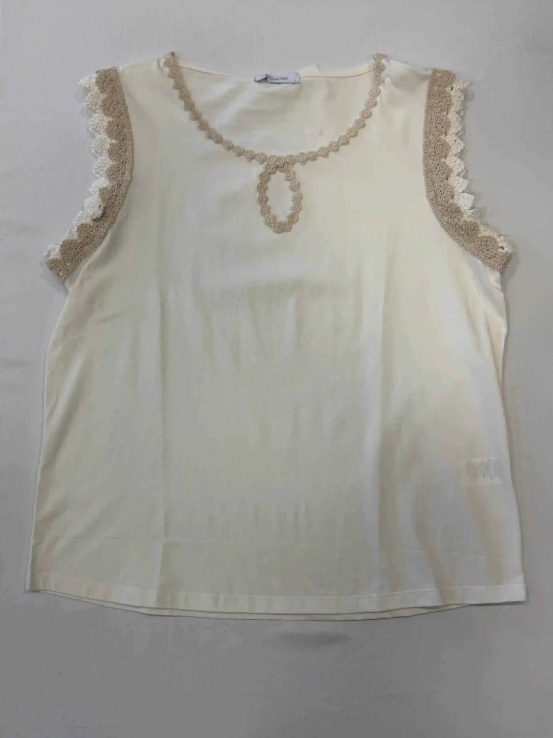 Blusa color crema sin mangas con detalles de encaje en los hombros y el escote sobre un fondo liso.