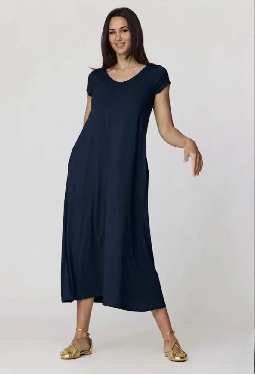 Mujer con vestido midi azul marino y sandalias doradas posando sobre un fondo claro liso.