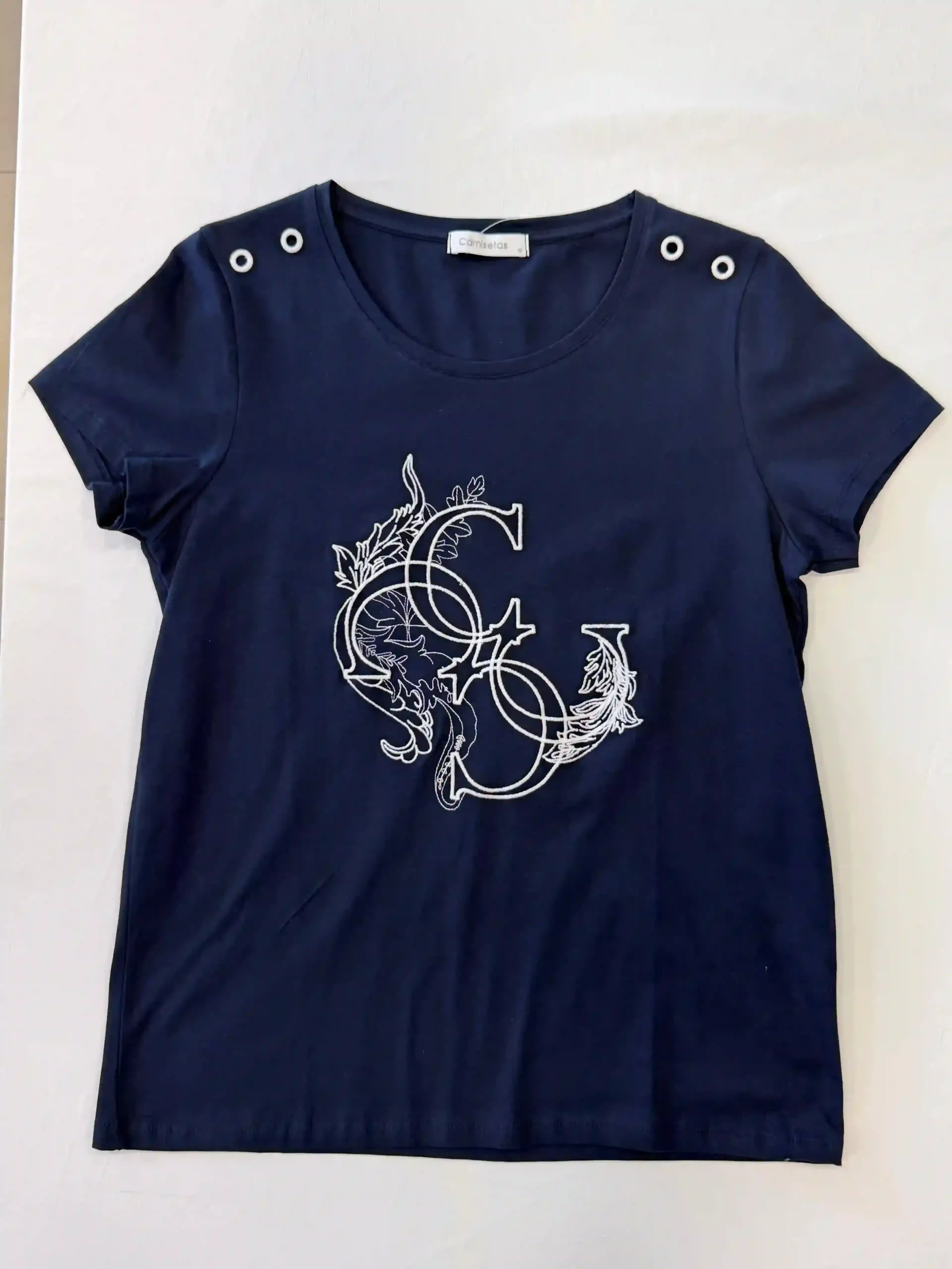 Camiseta azul marino con diseño floral blanco en forma de media luna y detalles de ojales en los hombros.