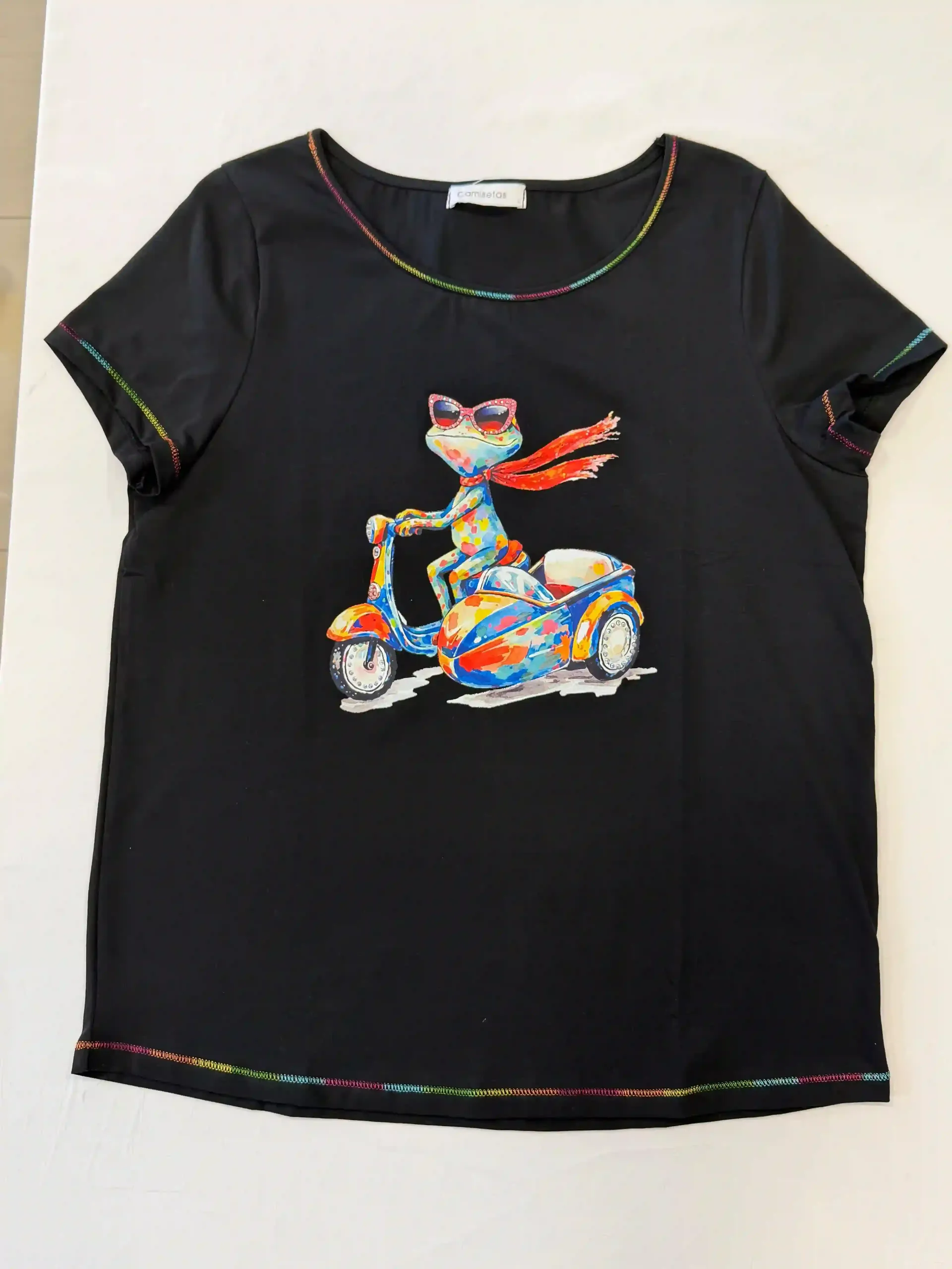 Camiseta negra con un colorido dibujo animado de una moto y su conductor, cuello y dobladillo con ribete de arcoíris.