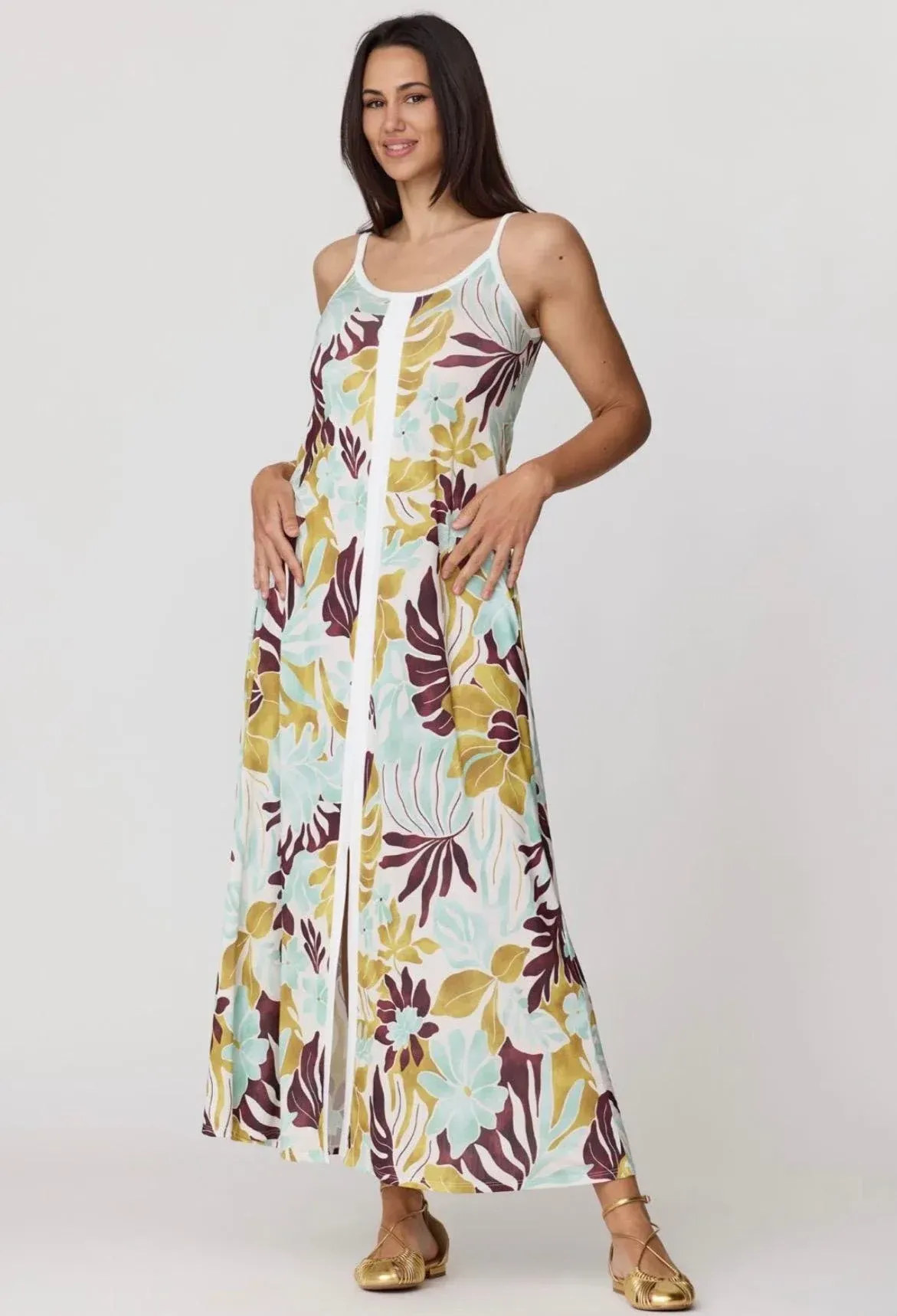 Mujer con un vestido largo blanco estampado de flores y sandalias, de pie sobre un fondo gris claro.