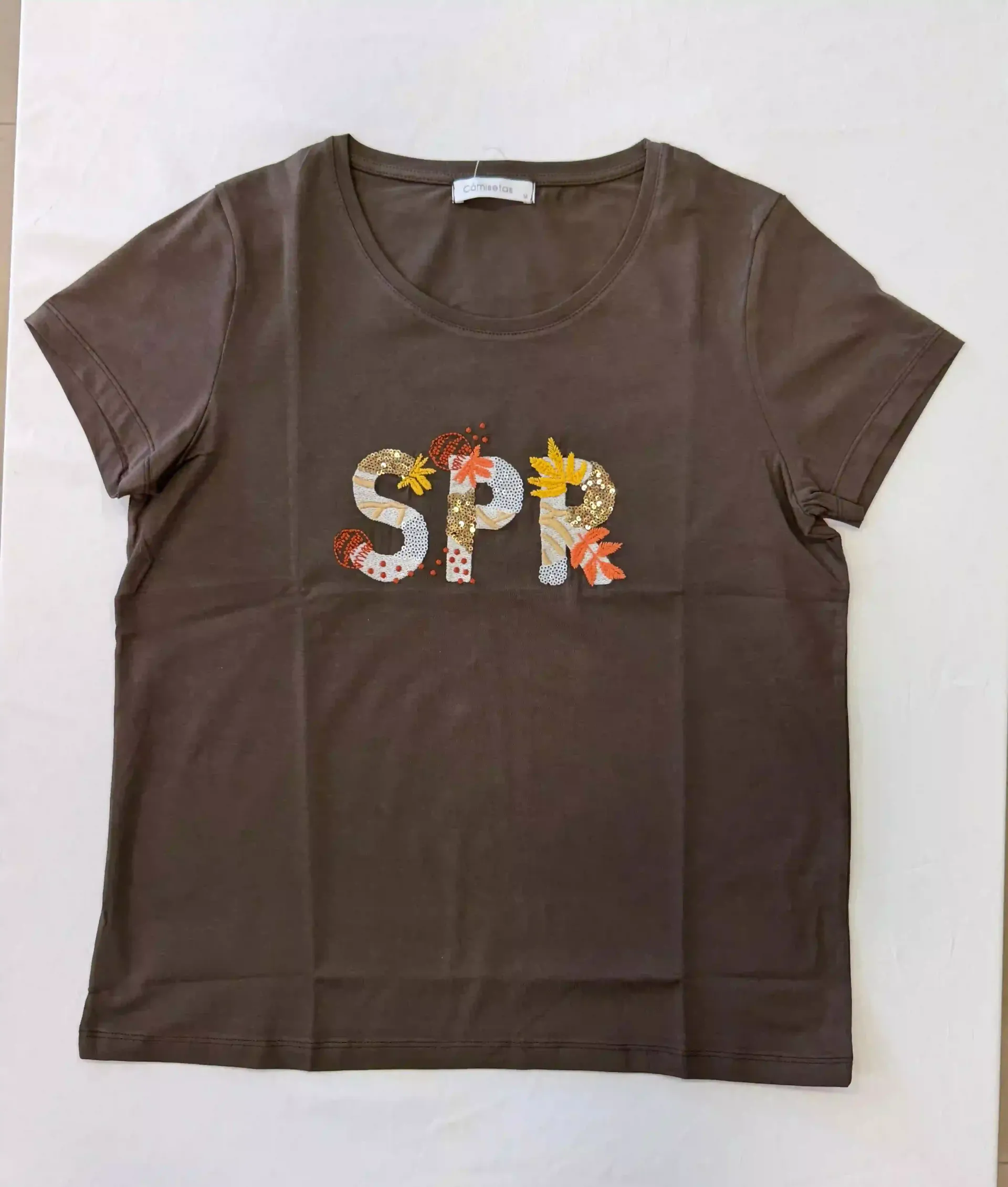 Camiseta marrón con letras florales coloridas “SPX” centradas en el pecho.