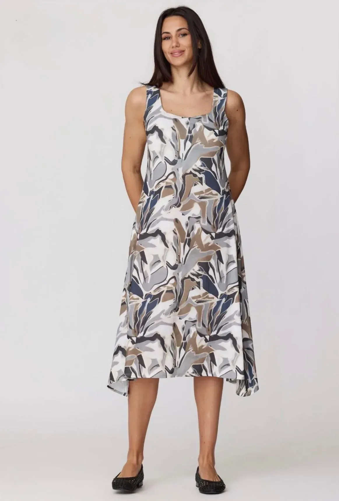 Mujer de pie con un vestido midi floral sin mangas con bolsillos y zapatos planos negros sobre un fondo liso.