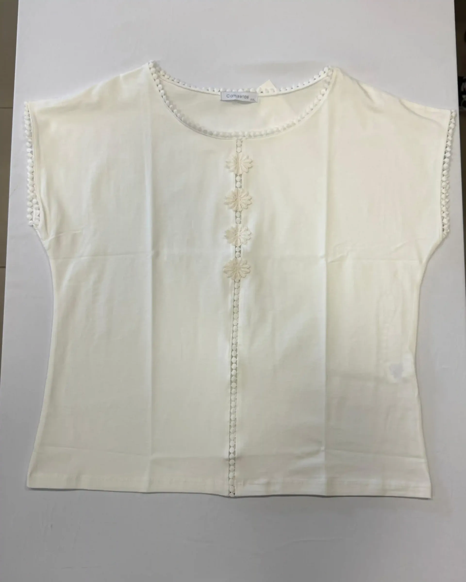 Blusa color crema de manga corta con botones en la parte delantera, extendida sobre un fondo blanco.