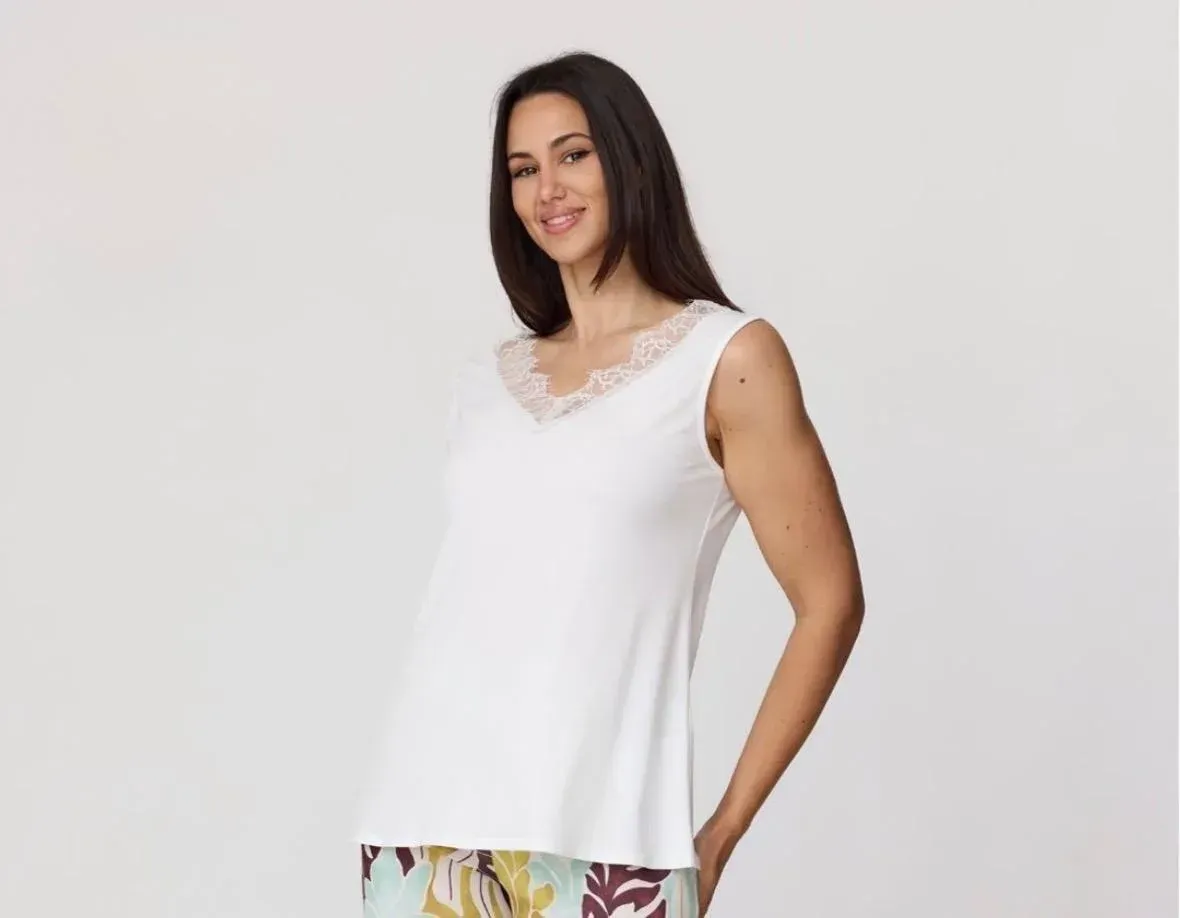 Mujer con top blanco sin mangas y pantalones estampados, sonriendo contra un fondo claro liso.