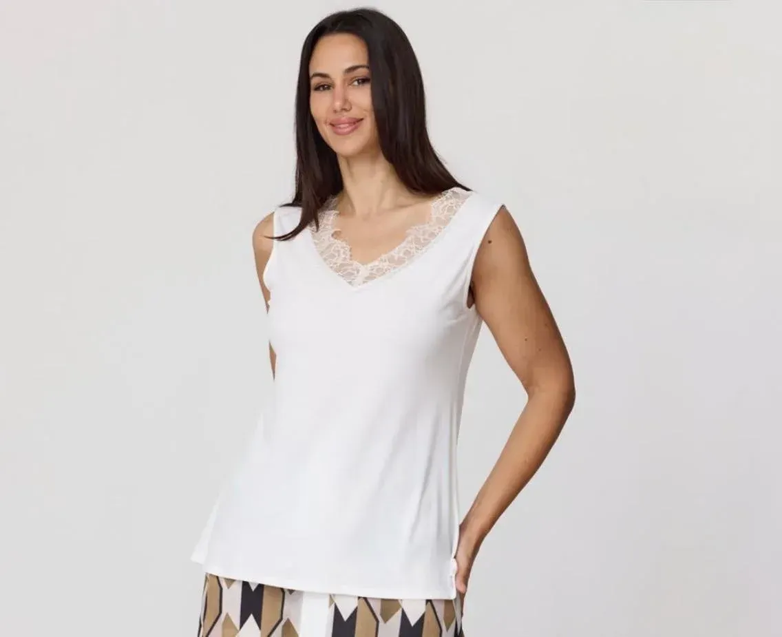 Mujer con una blusa blanca sin mangas con escote de encaje, de pie sobre un fondo gris claro.
