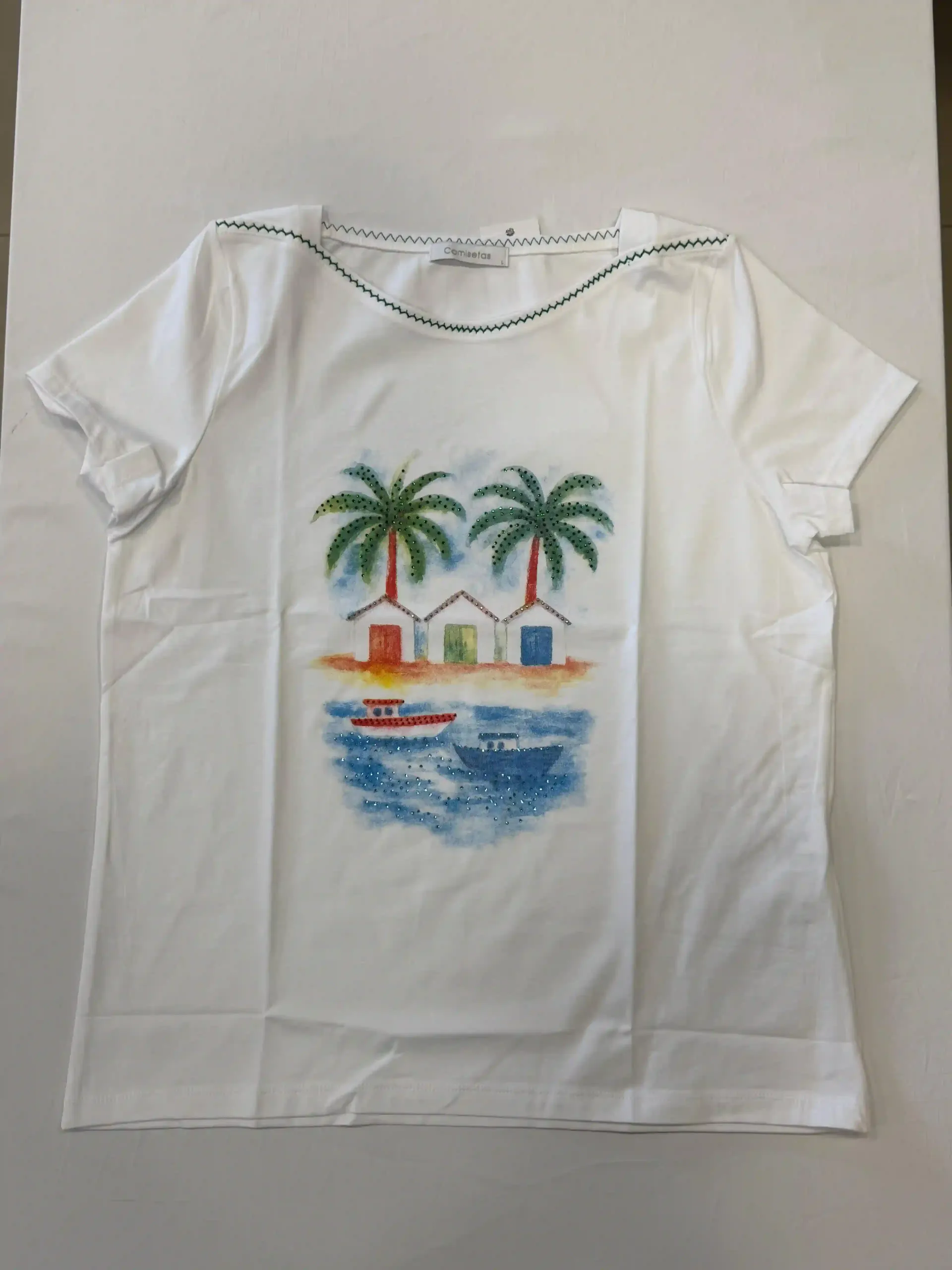 Camiseta blanca con estampado de palmeras y escena de playa en la parte delantera.