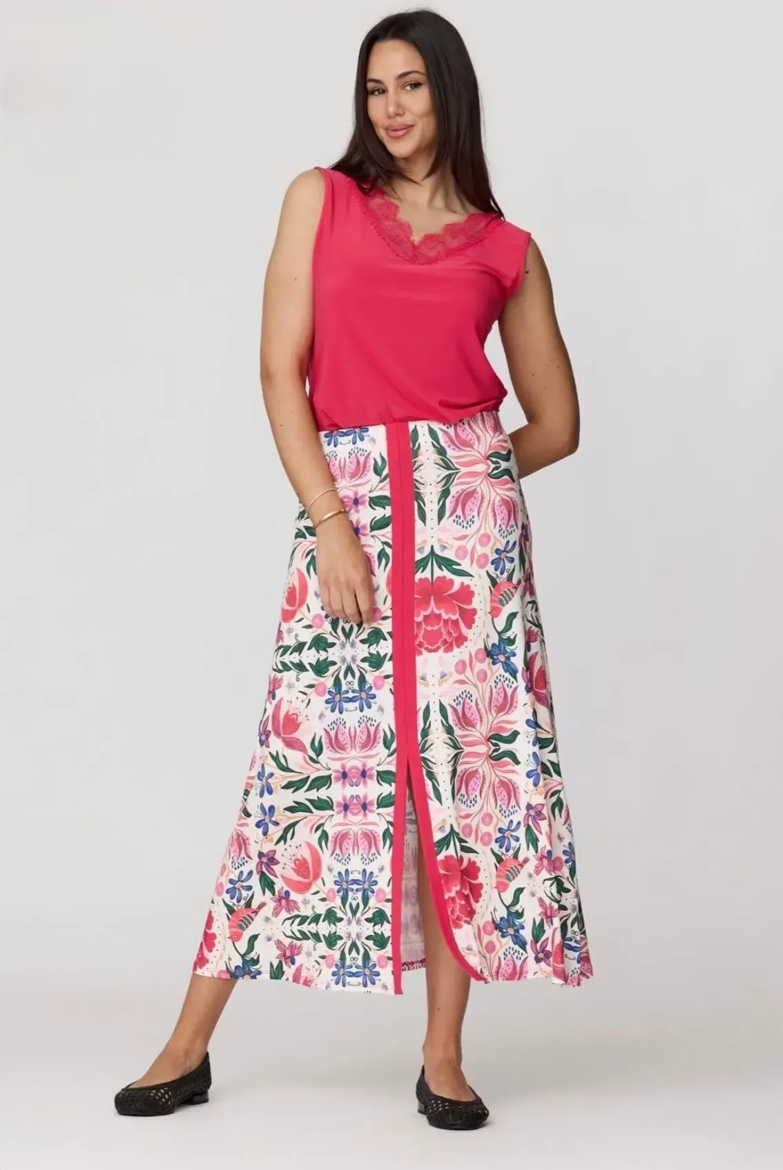 Mujer con top rosa y falda floral posando en un estudio con zapatos planos negros.