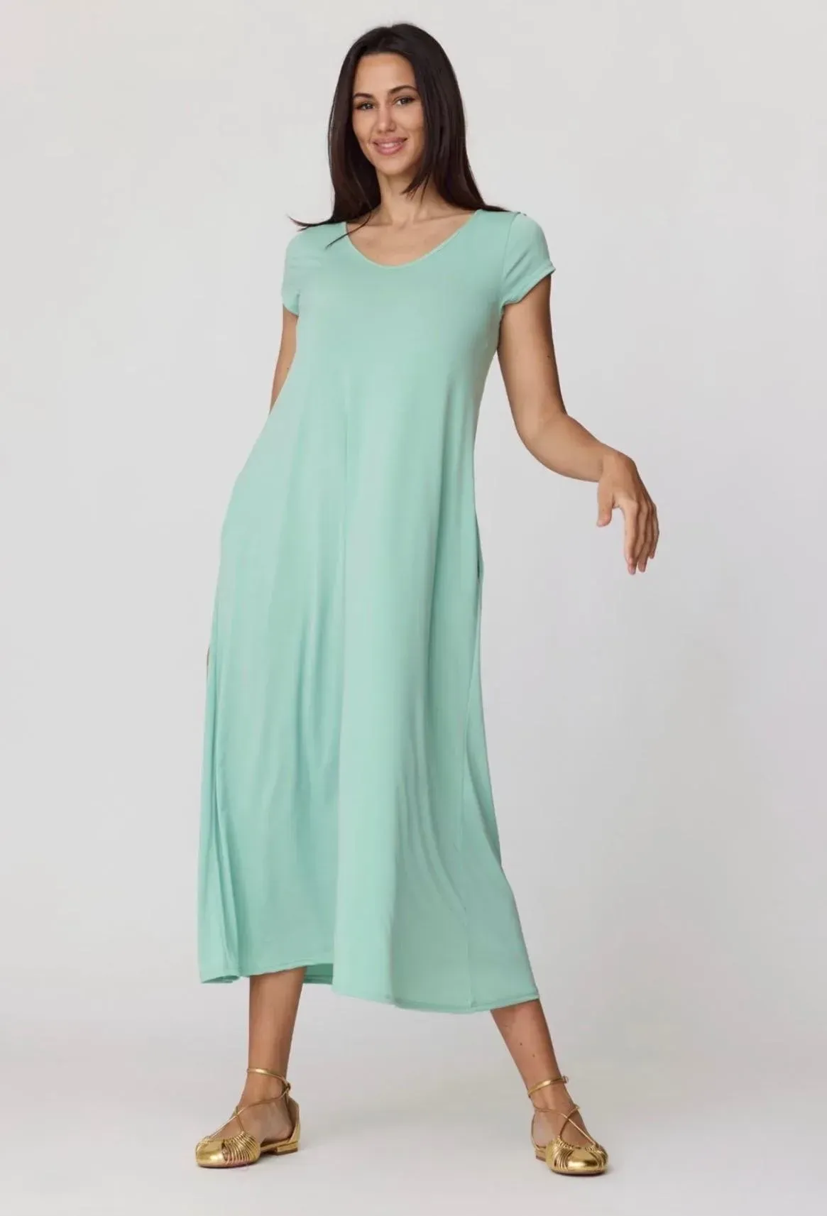 Mujer modelando un vestido midi sin mangas de color verde menta y sandalias doradas sobre un fondo claro.