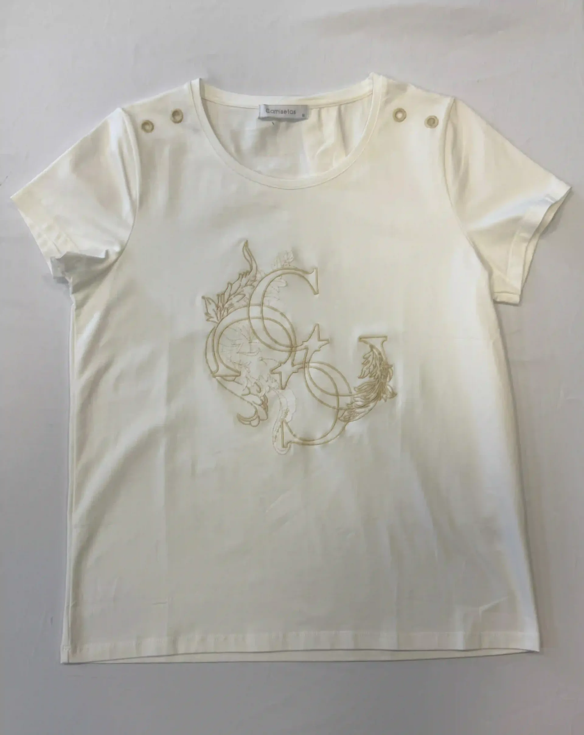 Camiseta blanca de manga corta con bordado floral dorado y detalles de botones en los hombros.