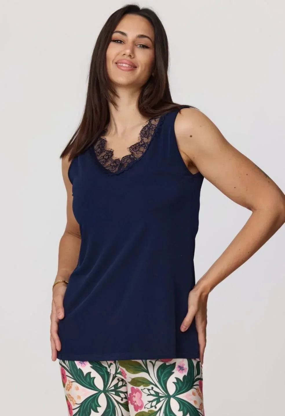 Mujer con top azul marino sin mangas y pantalones estampados de flores, posando frente a un fondo claro.