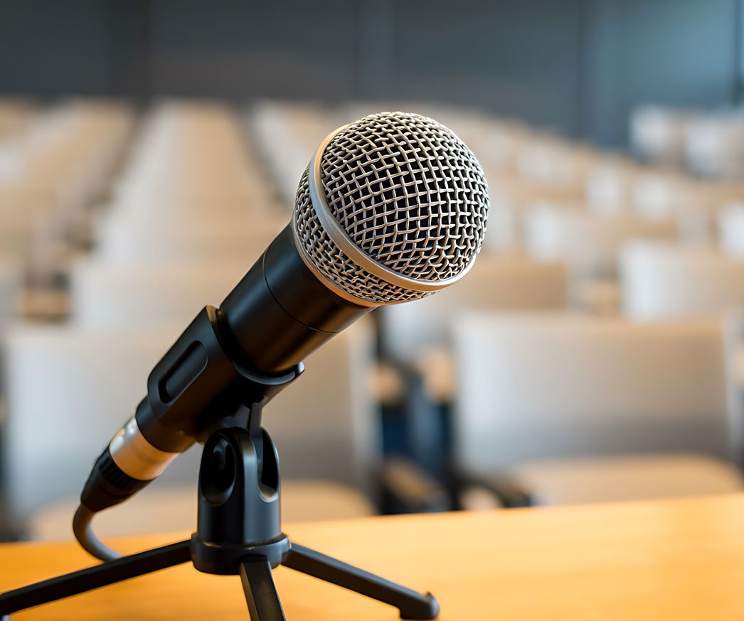 Un microphone sur un trépied, dans un auditorium vide aux chaises blanches.