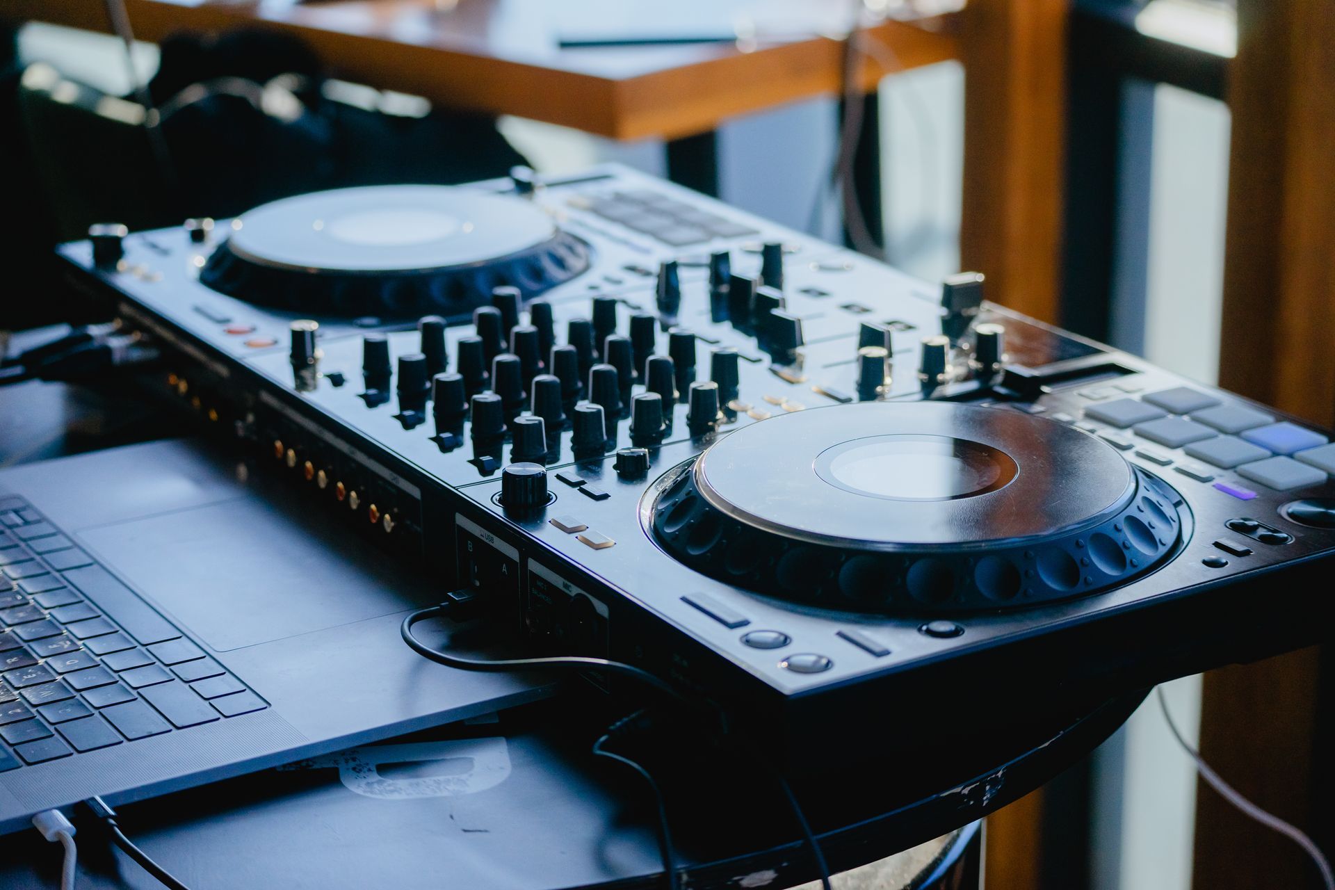 Contrôleur DJ avec ordinateur portable, vue en angle. Argent et noir, avec plusieurs boutons et deux plateaux tournants circulaires.