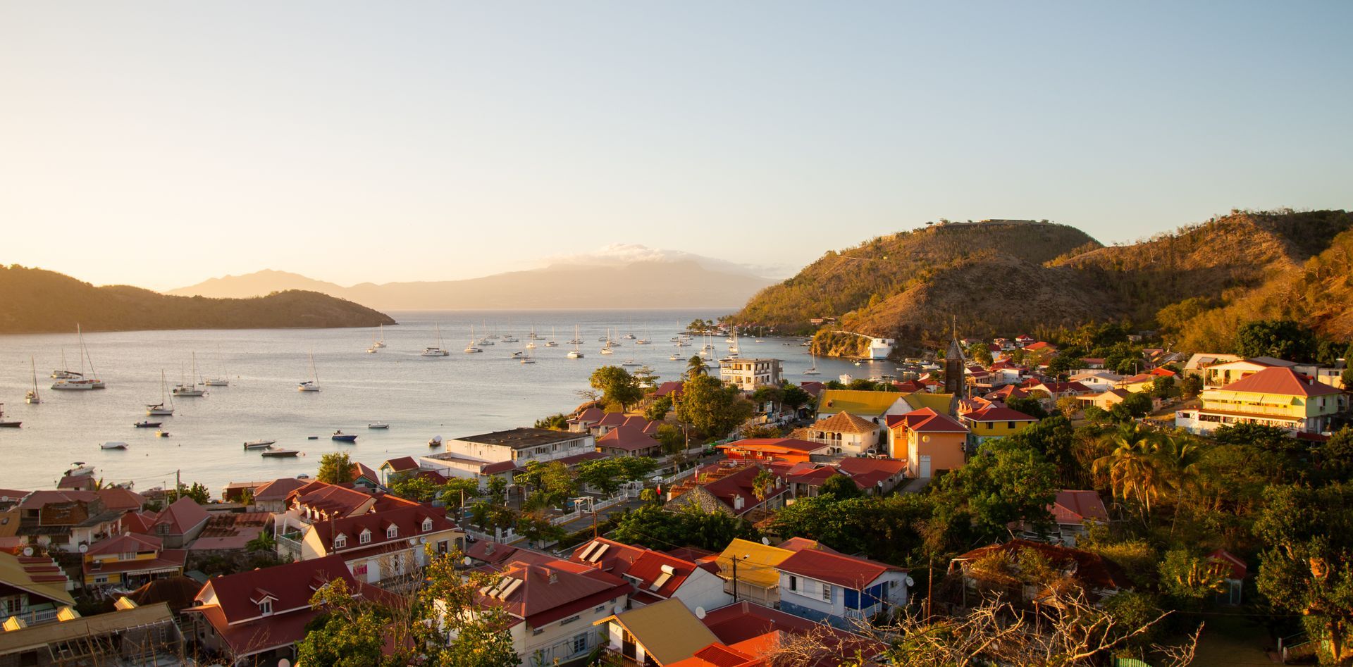 Ville côtière aux bâtiments colorés, aux bateaux et aux collines sous un ciel dégagé.