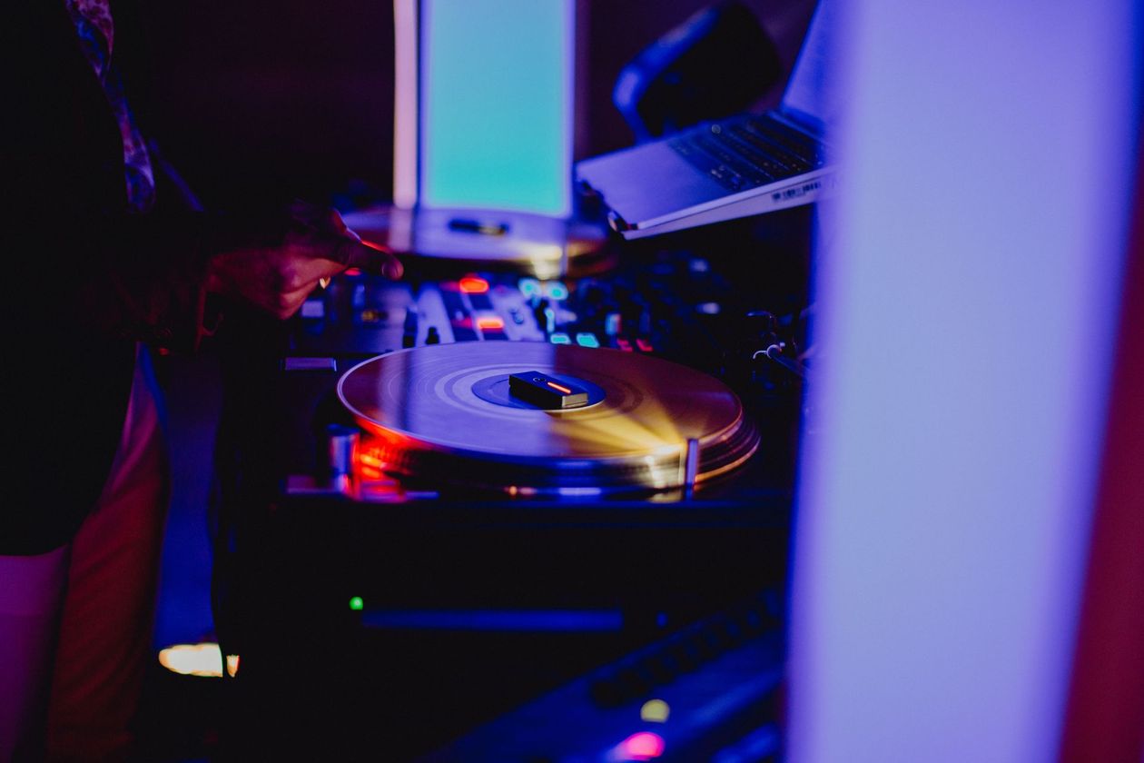 DJ au travail, la main sur une platine vinyle, mixant de la musique. Pièce sombre, lumières colorées.