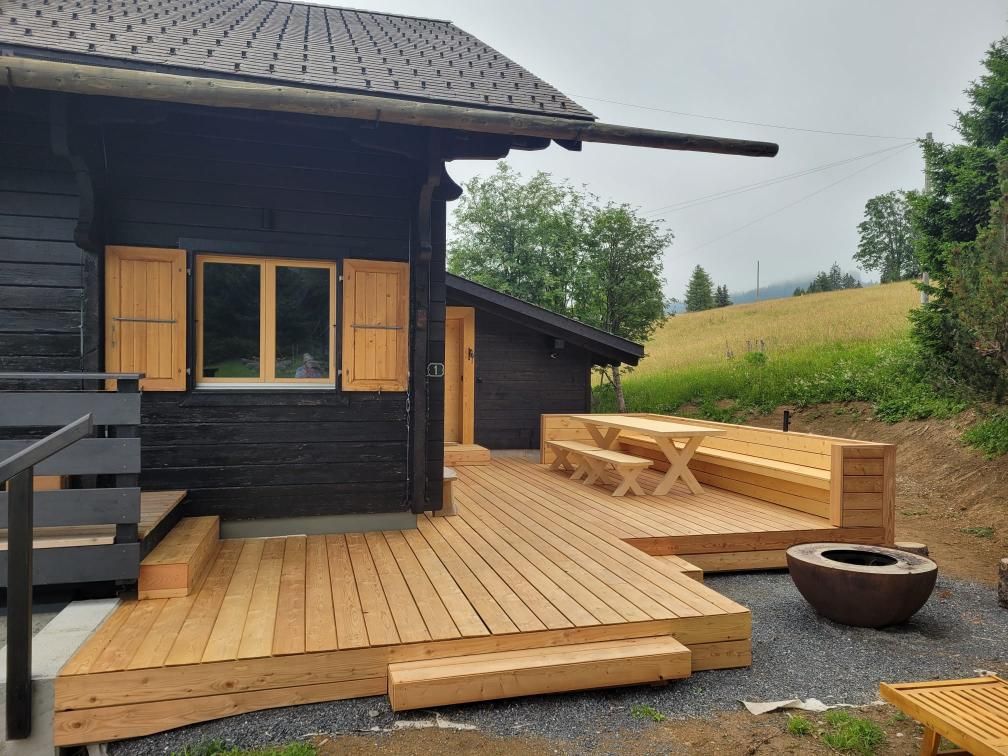 Une maison noire avec une terrasse en bois et une table de pique-nique