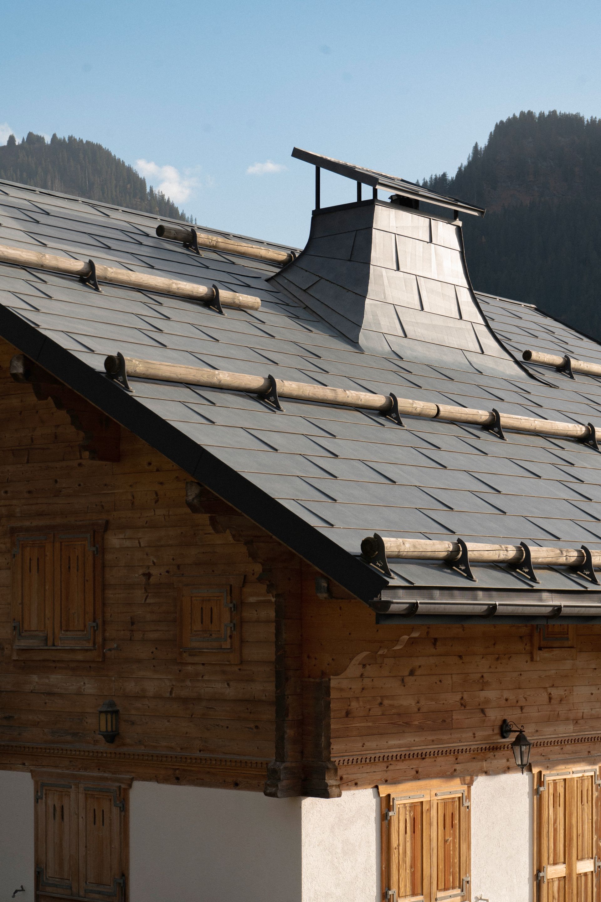 Une maison en bois avec un toit en ardoise et des montagnes en arrière-plan
