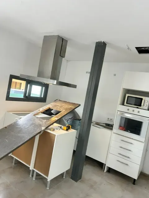 Cocina con una encimera inclinada junto a una campana extractora de acero inoxidable, una viga de soporte negra y hornos apilados.