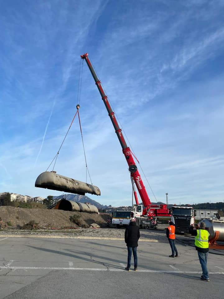 une grue soulevant une moitié de tuyau industriel