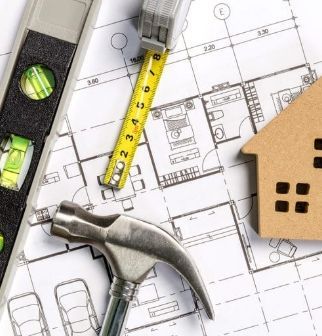 Marteau, mètre ruban, niveau et silhouette de maison sur un plan d’architecte.