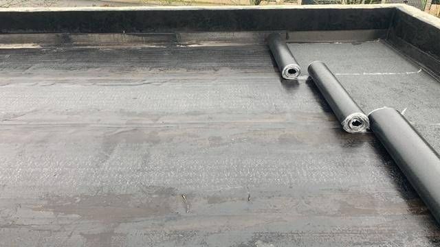 Toit-terrasse gris avec des tuyaux noirs et un étroit caniveau de drainage le long du bord
