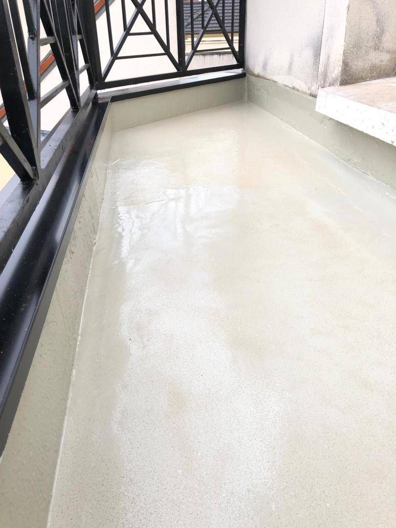 Balcon avec un sol blanc mouillé, une rambarde noire et des rideaux près d’une porte-fenêtre