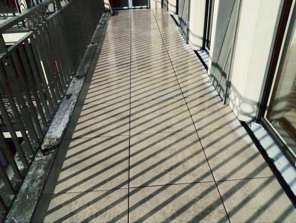 Allée extérieure ensoleillée, traversée par des ombres rayées au sol et des ombres de rambarde sur le côté.