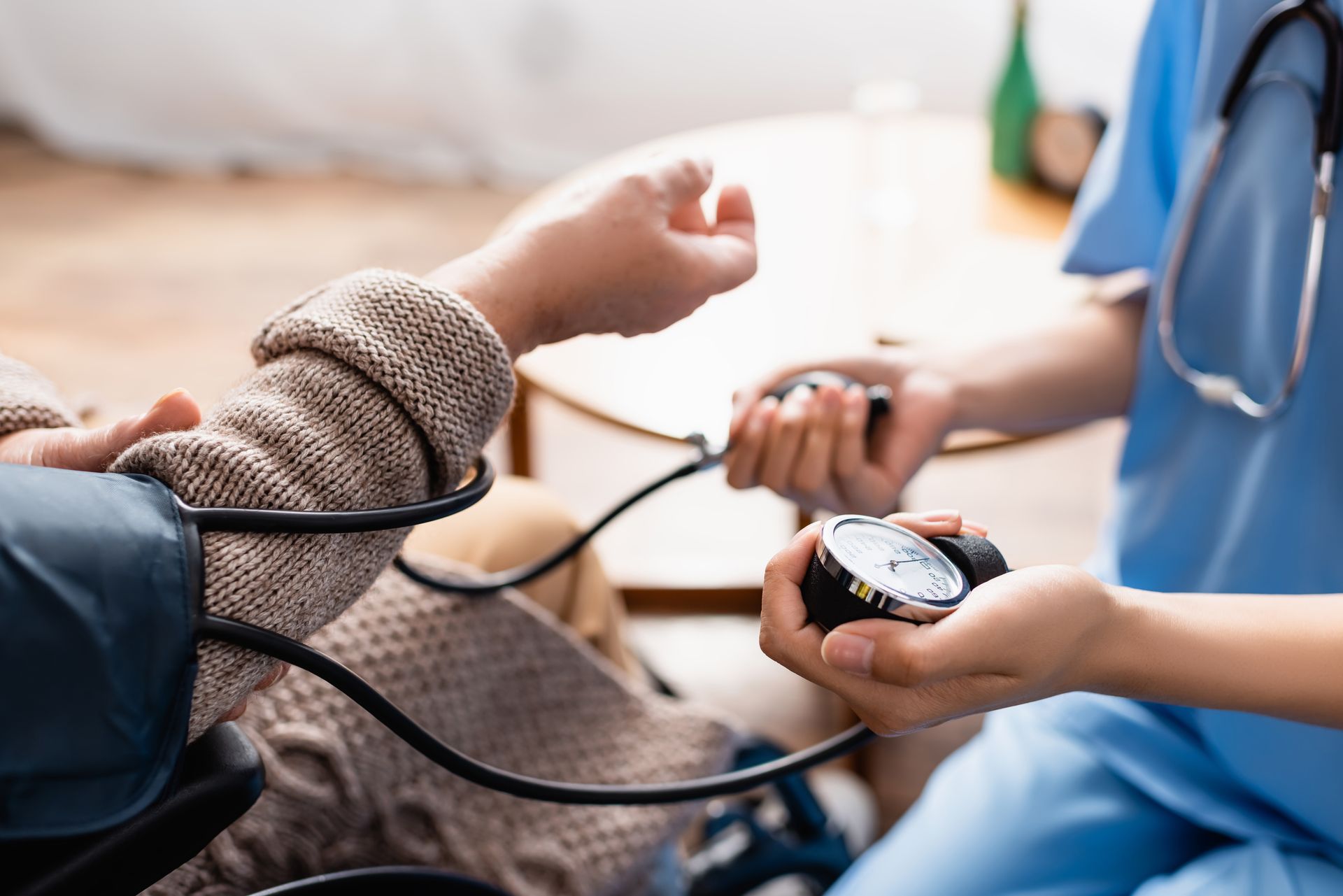 Une infirmière prend la tension artérielle d'un patient âgé avec un stéthoscope et un brassard à domicile.