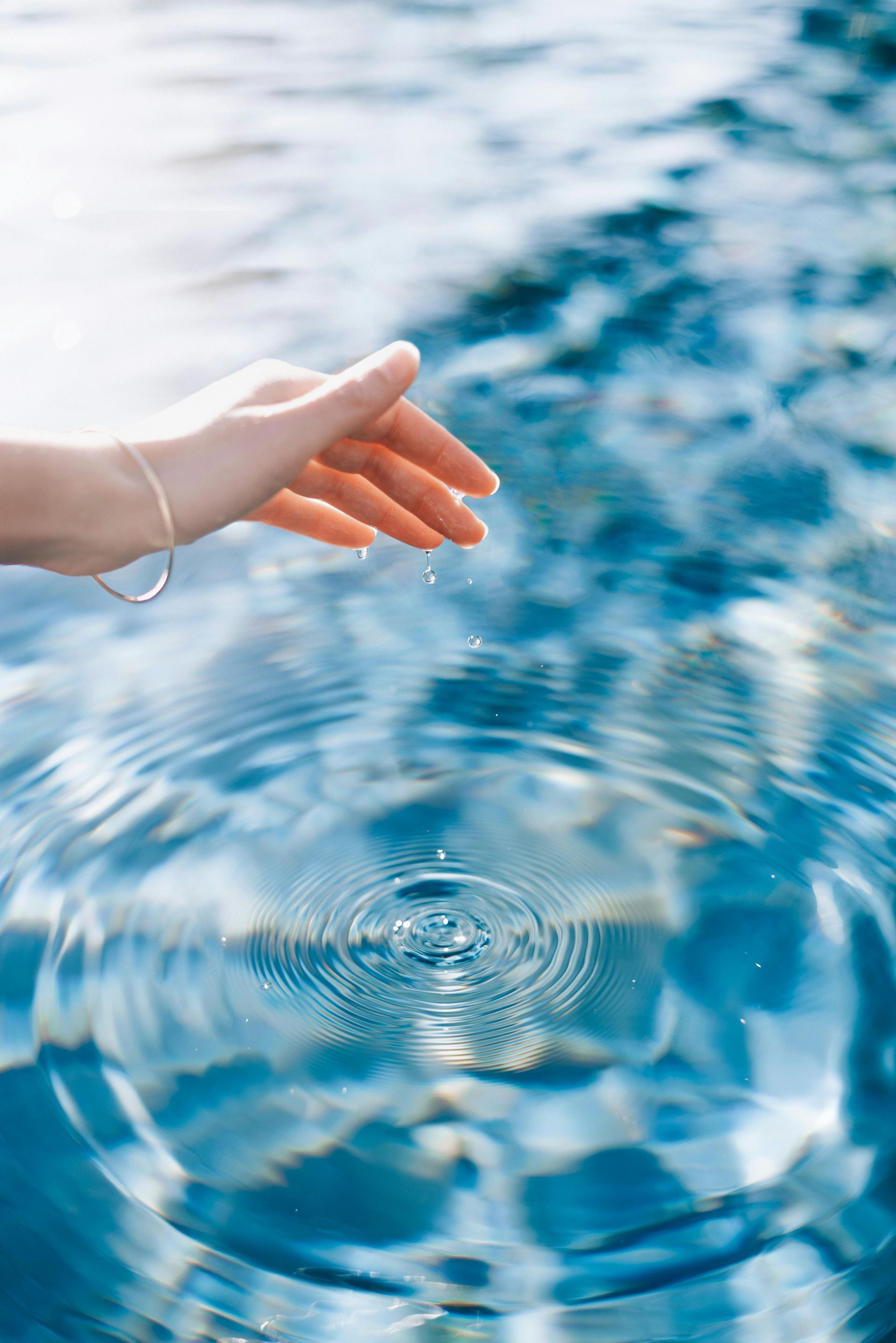 Une main tendue vers l'eau bleue ondulante aux vagues circulaires