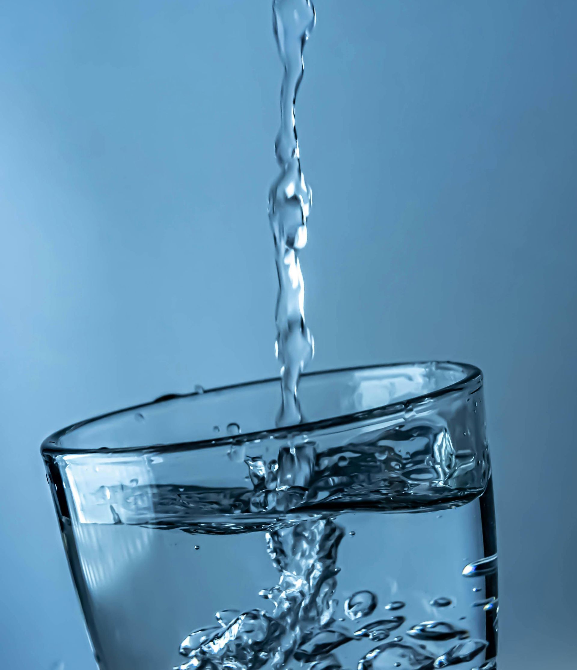 De l'eau se déverse dans un verre transparent sur fond bleu.