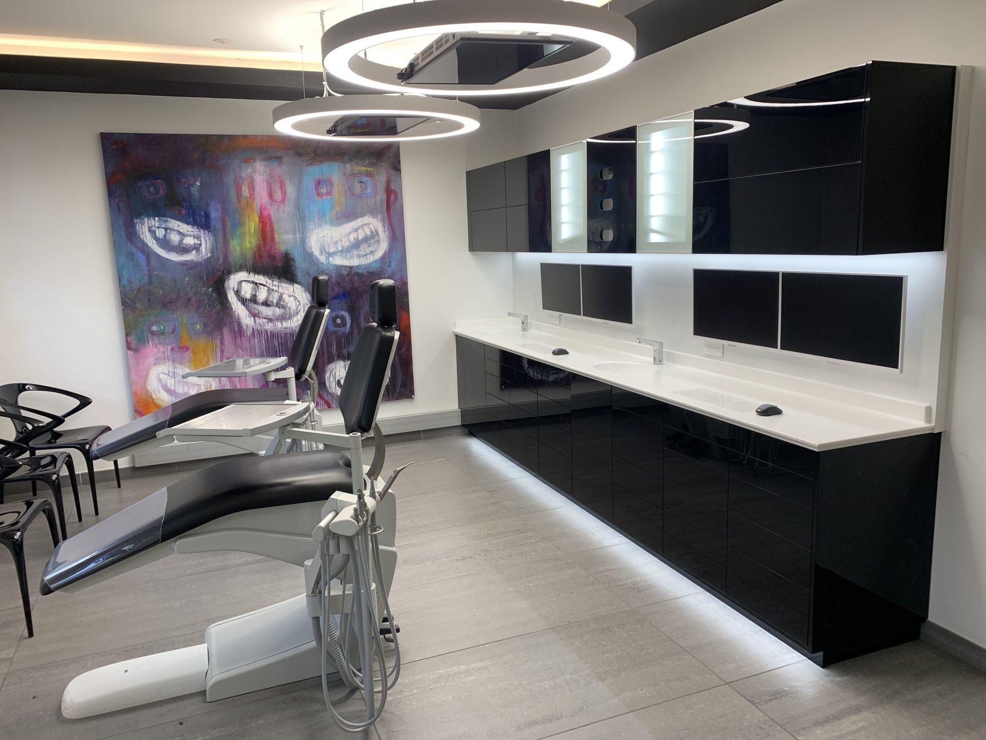 Cabinet dentaire moderne avec deux fauteuils inclinables pour les patients, meubles noirs, comptoirs blancs et œuvres d'art abstraites.