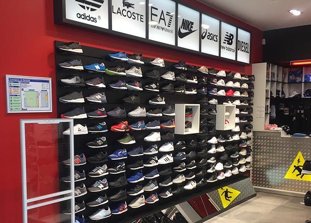 Présentoir mural de magasin avec des rangées de baskets de sport variées, mises en valeur par des logos de marques illuminés sur un fond rouge vif.