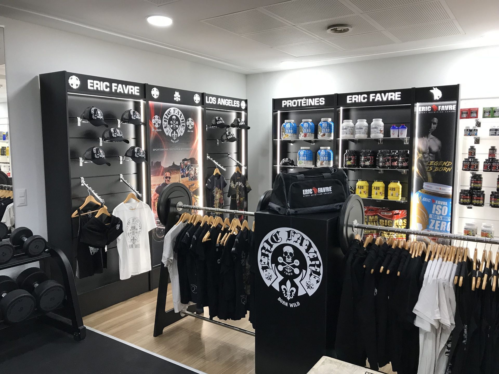 Un présentoir dans une salle de sport mettant en avant les compléments nutritionnels sportifs, les vêtements et les équipements sportifs de la marque Eric Favre.