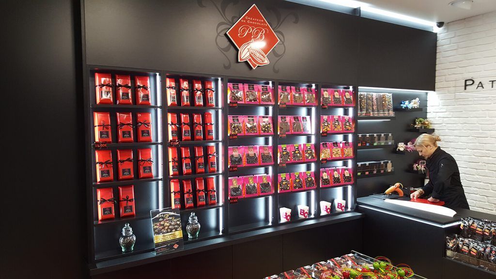 L'intérieur d'un magasin avec des étagères remplies de chocolats emballés et un employé travaillant derrière un comptoir.