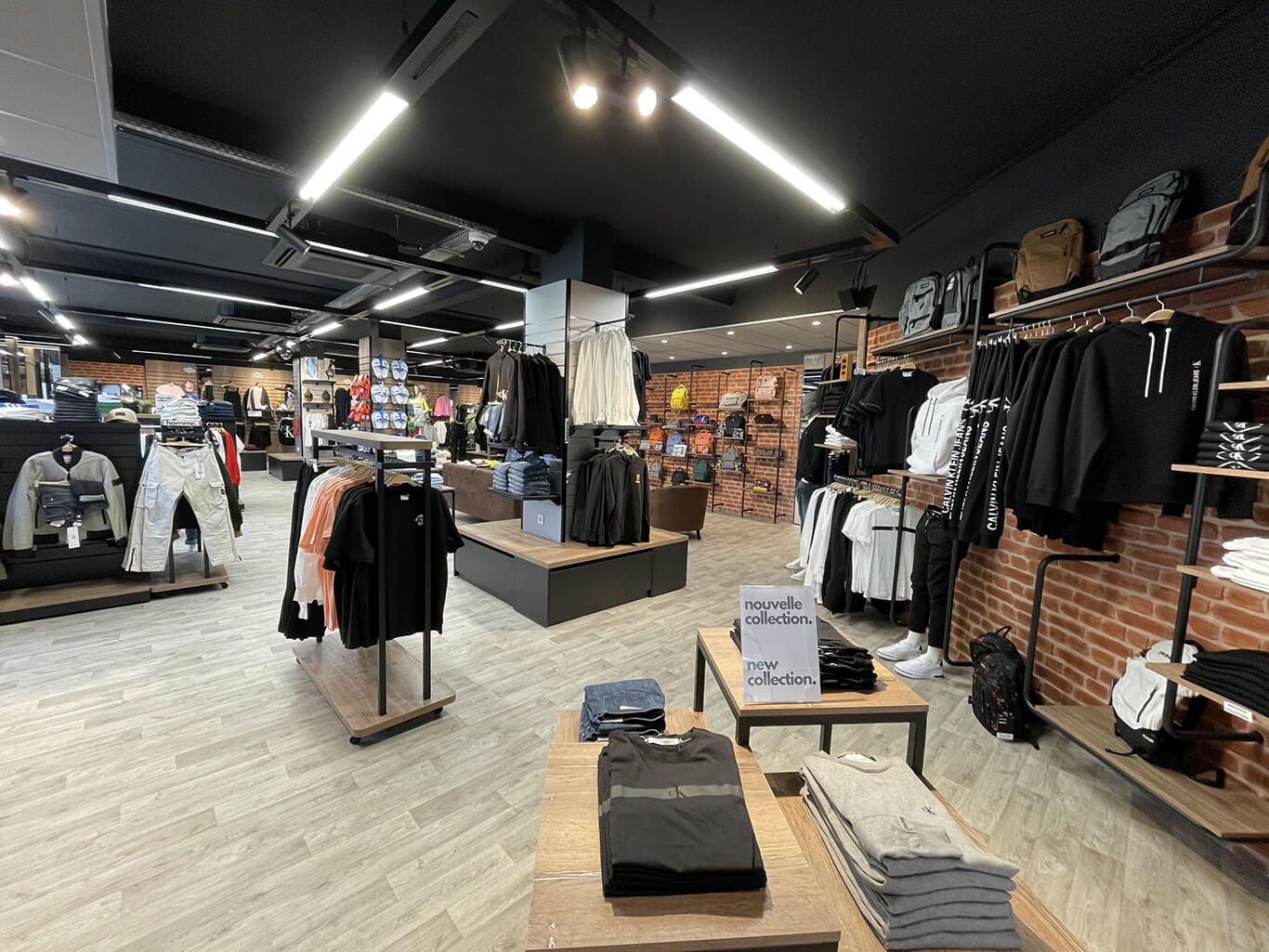Un magasin de vêtements présentant des rangées de vêtements sur des portants et des étagères, avec des présentoirs en bois et un mur de briques apparentes.