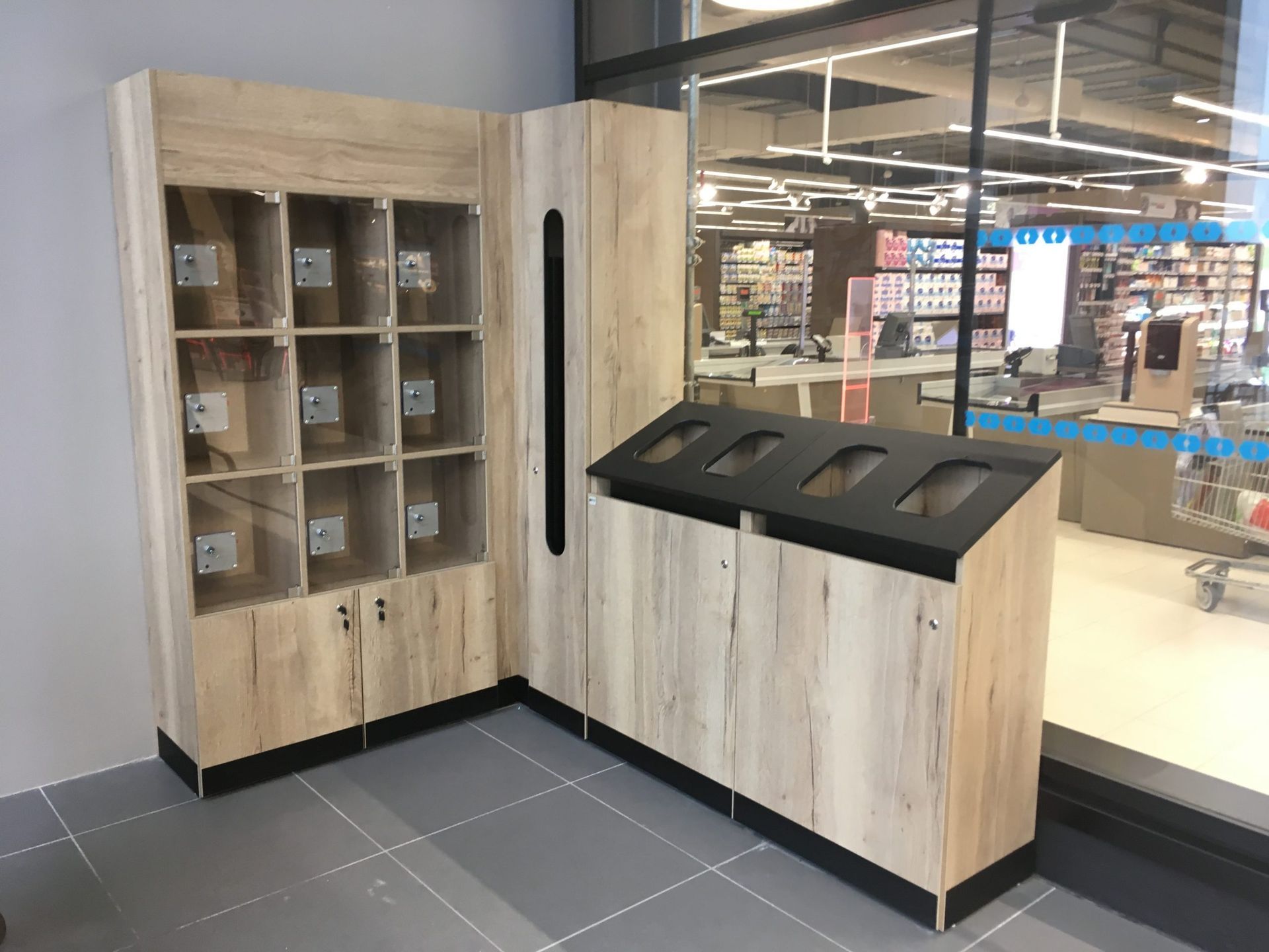 Des casiers de rangement en bois clair avec portes vitrées jouxtent une station de tri des déchets assortie, équipée de quatre fentes de dépôt.