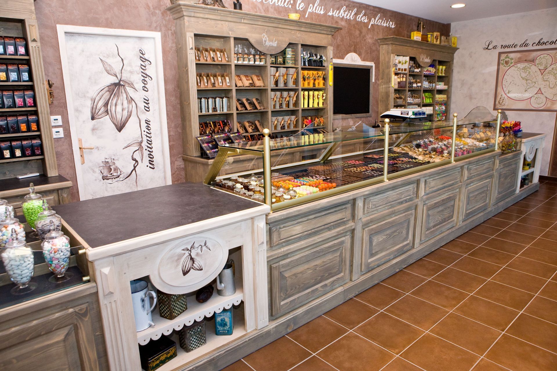 Une chocolaterie de charme avec un long comptoir vitré, des étagères remplies de confiseries et un décor rustique.