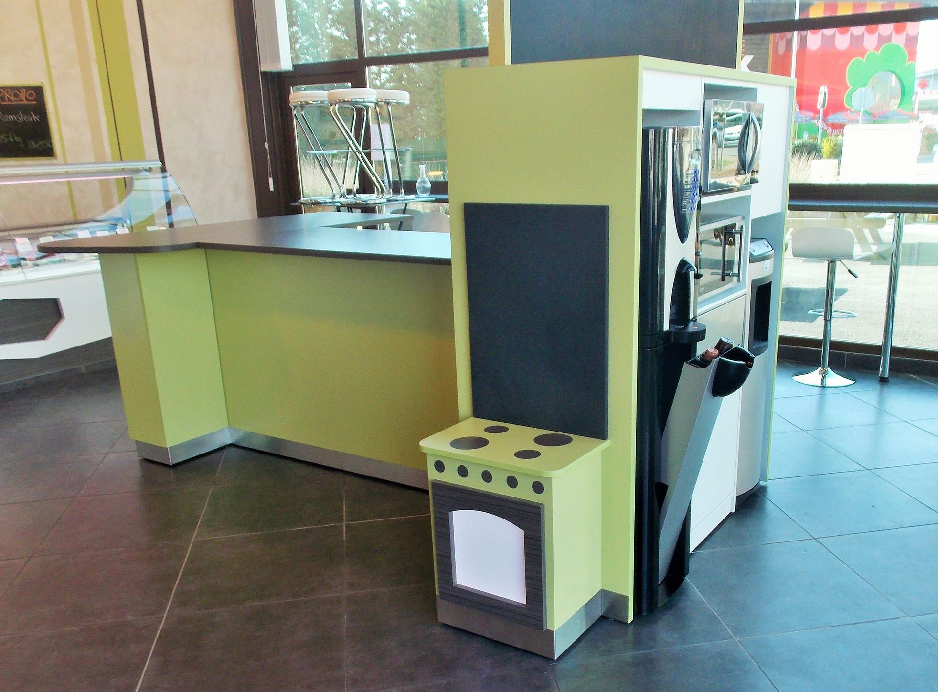 Un îlot de cuisine miniature vert citron avec une cuisinière peinte et un tableau noir, le tout sur fond de comptoir de magasin.