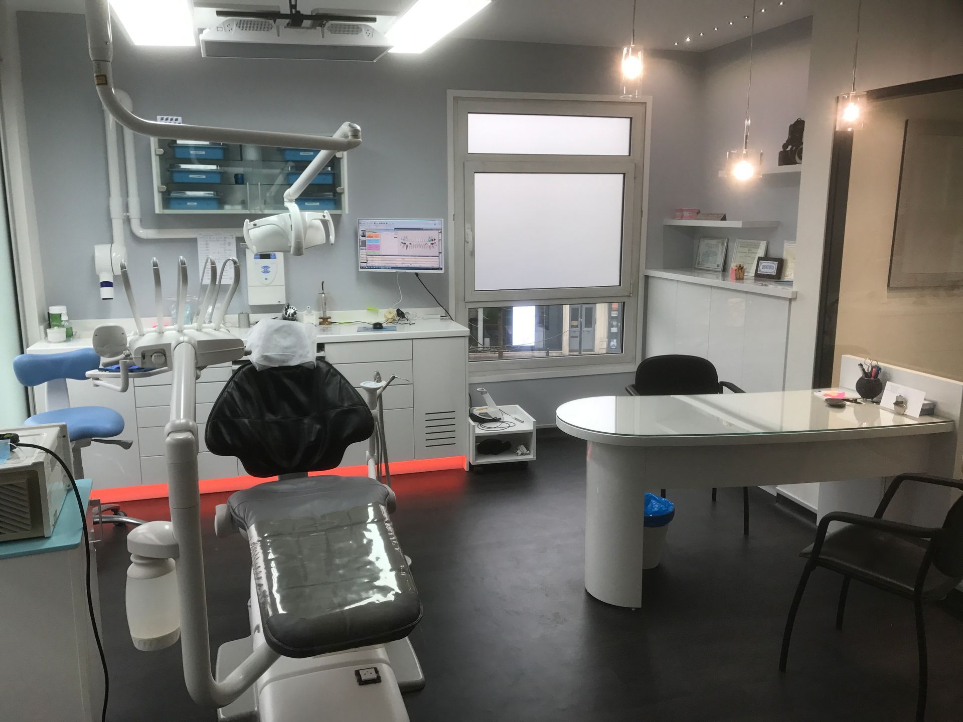 Une clinique dentaire moderne avec un fauteuil dentaire, du matériel médical et un bureau dans une pièce aux couleurs neutres.