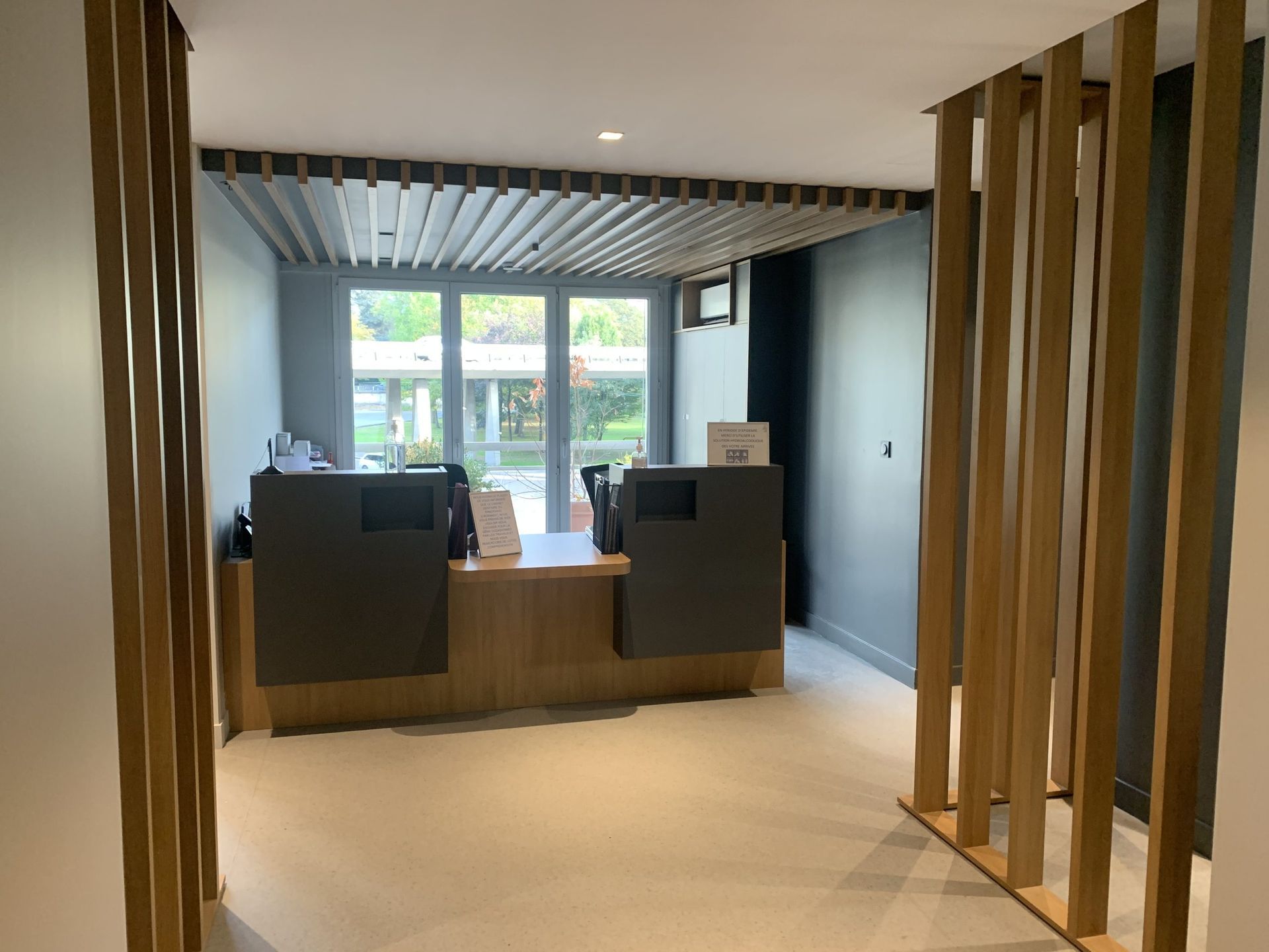 Un espace d'accueil comprenant un bureau, des murs gris foncé, des cloisons et un plafond décorés de lattes de bois.