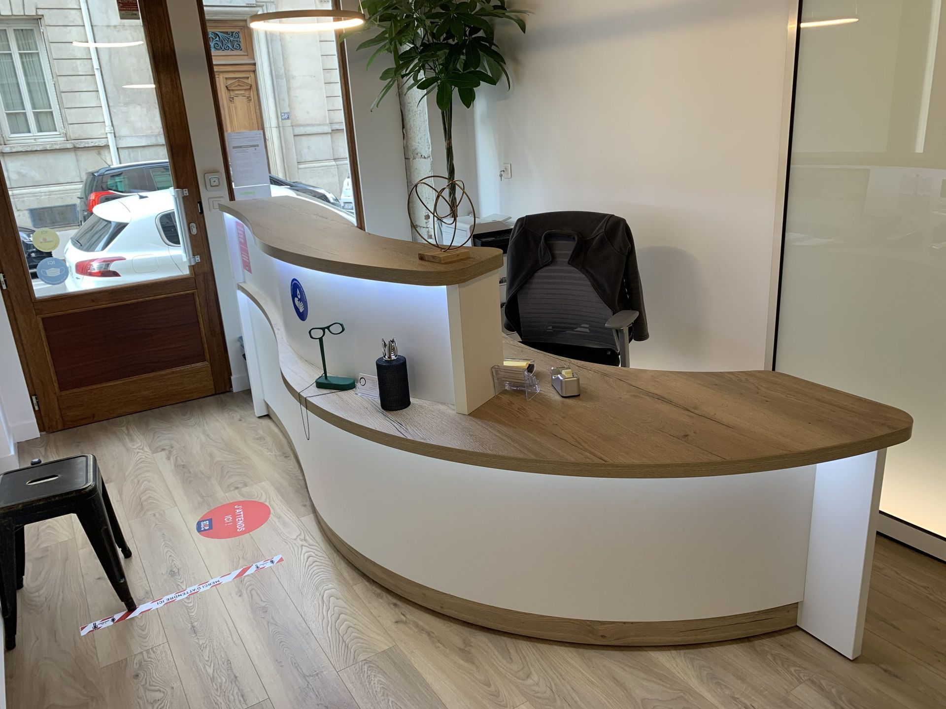Un comptoir d'accueil moderne et incurvé, avec un plateau en bois clair et un piètement blanc, dans une entrée de bureau lumineuse.