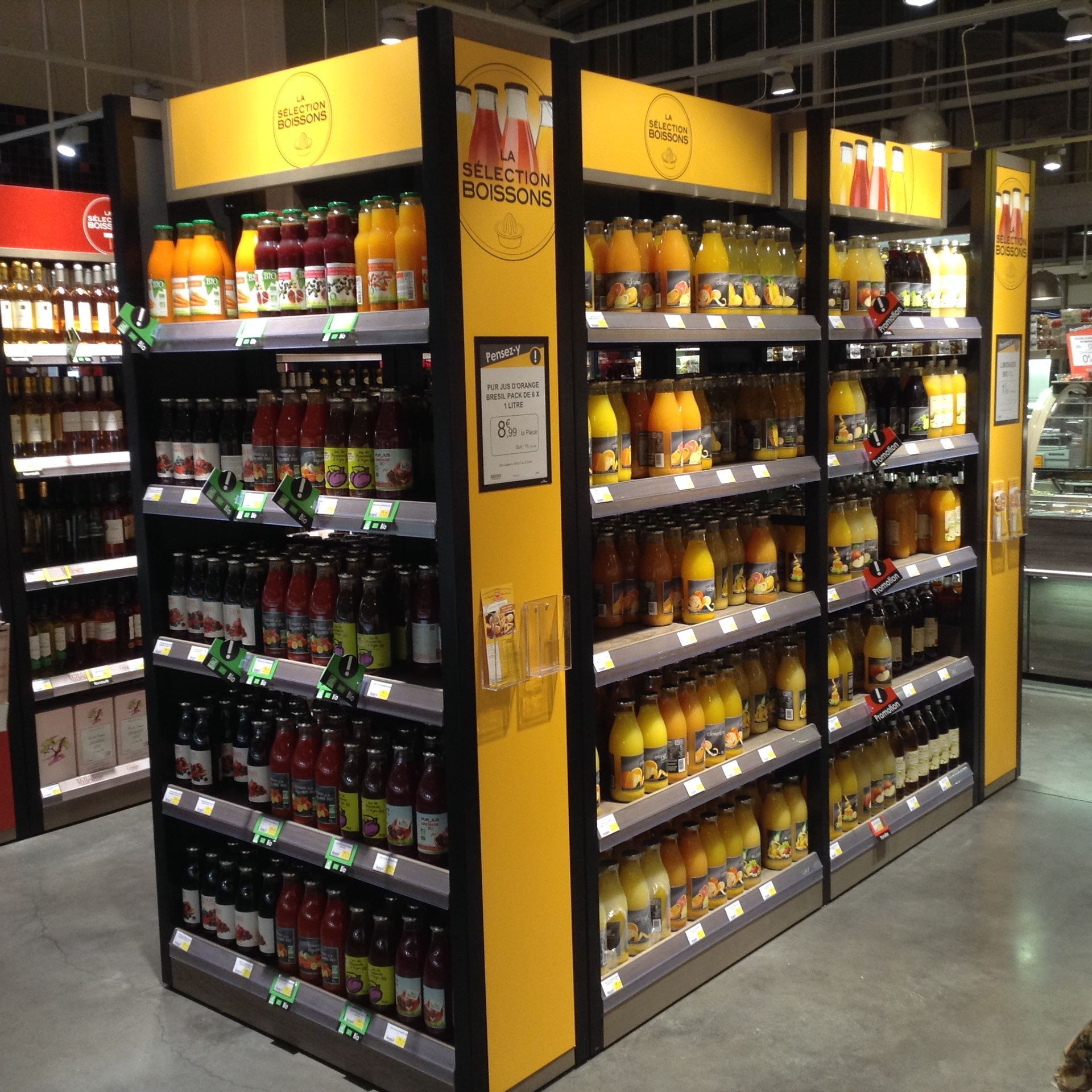 Un présentoir de rayon bien garni, aux accents jaunes, présentant diverses bouteilles de jus, dans une allée de supermarché.